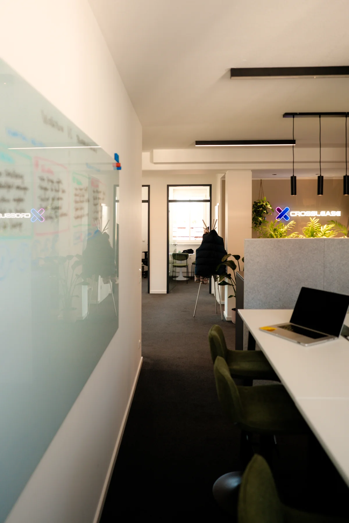 Blick in das CrossLease Büro mit Glassboard, Arbeitsplätzen und Brand-Neon-Logo