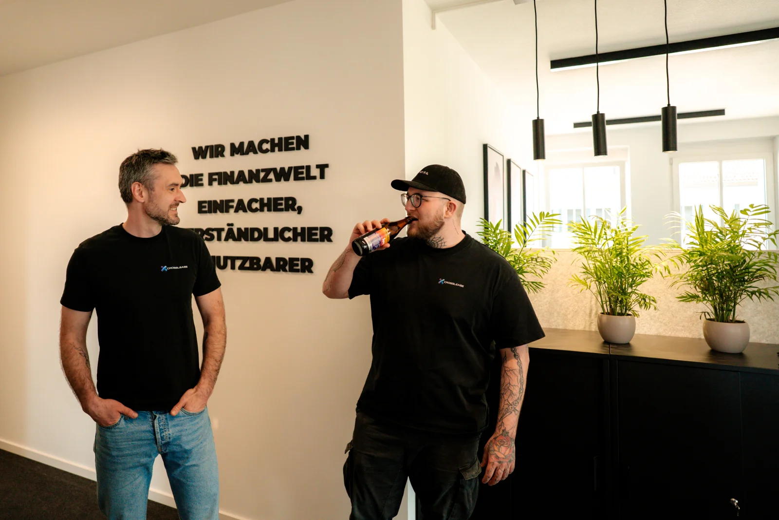 Zwei CrossLease Mitarbeiter im Gespräch vor der Slogan-Wand im Büro